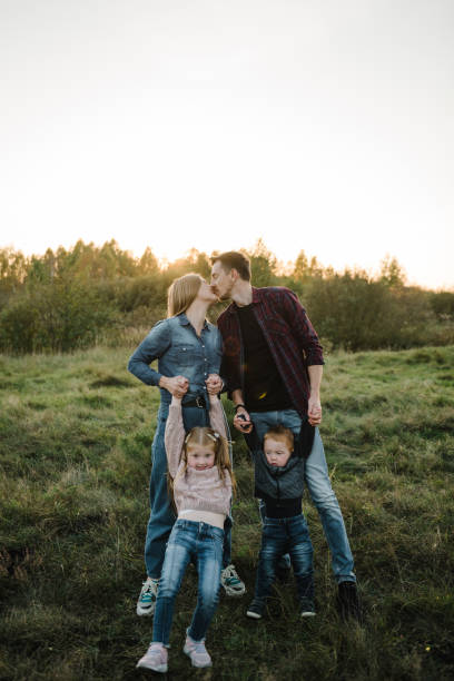 Family spending time together in nature. Parents hold in hands and hugs happy kids in autumn day. Mother, father, daughter, son walks in grass in spring field at sunset. Childs embrace parents. familia pasando tiempo juntos en la naturaleza. los padres se toman de las manos y abrazan a los niños felices en el día de otoño. madre, padre, hija, hijo camina en la hierba en el campo de primavera al atardecer. los niños abrazan a los padres.
