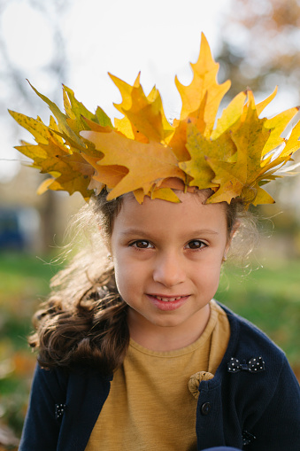 Beautiful little girl wearing autumn wreath made from dry maple leafs , sitting on the lawn