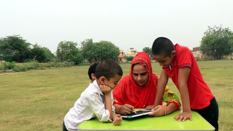 Indian mother teaching elementary children at home in garden using chalkboard portrait together.