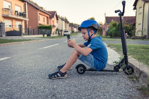 Adorable little boy sitting on his scooter using a smart phone.