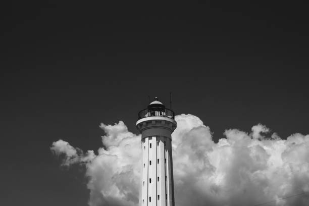 A monochromatic image of a small lighthouse, standing tall against a cloudy sky.