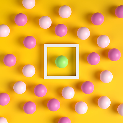 Green ball in a white frame surrounded by pink balls outside the box on yellow background. Difference, individuality, standing out from the crowd. Thinking outside the box. 3D render.