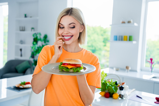 Photo of excited girl feel curious eating junk food delicious burger in white dining room.