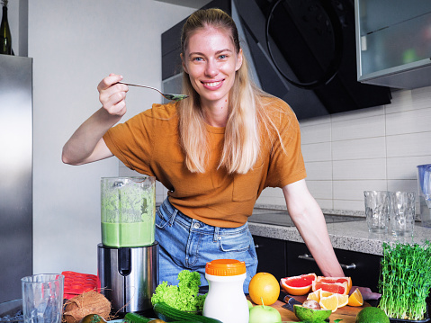 Beautiful young woman preparing a healthy smoothie with protein in a blender
