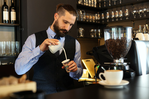 Young male bartender making cappuccino or espresso coffee in a bar. About 25 years old, Caucasian man.