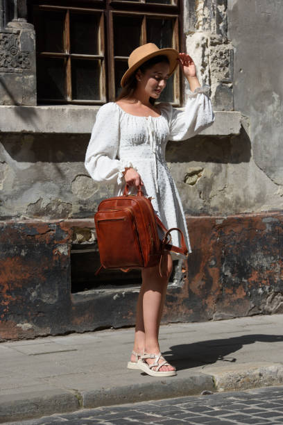 istock brunette wearing white romantic summer dress and beige hat posing with luxury leather backpack 1631335108