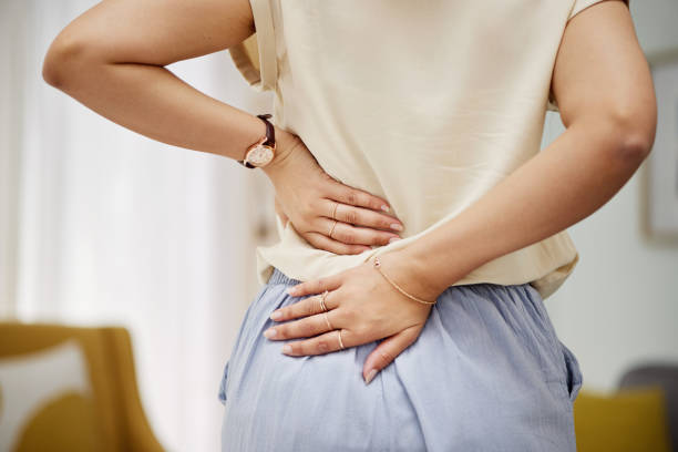 back pain, hands and woman in a living room with problem, discomfort or arthritis in her home. backache, spine and person with cramps, joint or posture in lounge with osteoporosis or fibromyalgia - dor de costas imagens e fotografias de stock