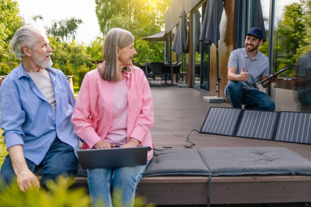 istock Man and woman sitting on house porch with solar panel using notebook. 1631345551