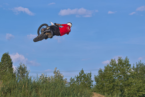 A male FMX freestyle motocross rider does a Tsunami trick off a big jump.