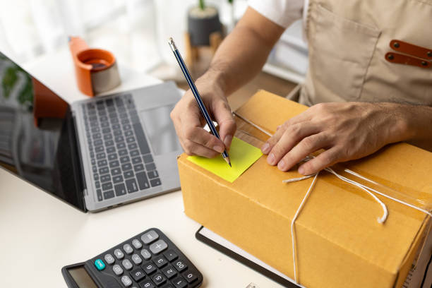 istock Man writing on parcel box, online shop owner checking orders from website on internet to confirm order with customers who ordered and pack products for delivery. Concept of selling products online. 1631361008
