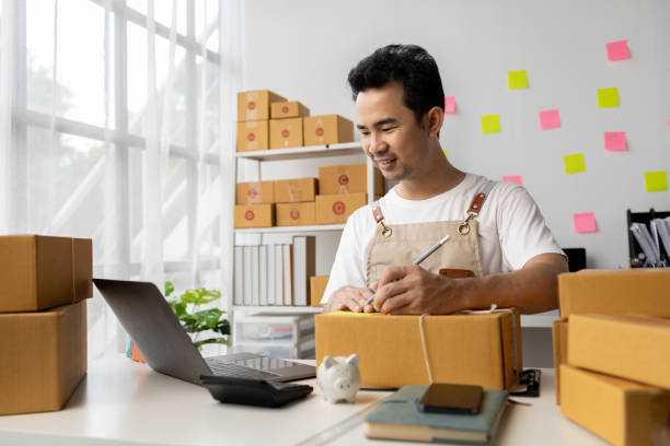 istock Man writing on parcel box, online shop owner checking orders from website on internet to confirm order with customers who ordered and pack products for delivery. Concept of selling products online. 1631361021