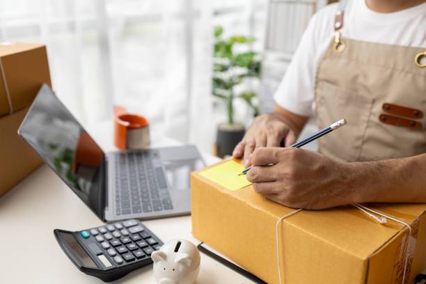 istock Man writing on parcel box, online shop owner checking orders from website on internet to confirm order with customers who ordered and pack products for delivery. Concept of selling products online. 1631361027