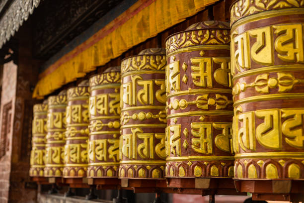 Prayer wheel along the mountain road to Swayambunat Temple in Kathmandu, Nepal Kathmandu is the capital of Nepal, known for its cultural heritage, temples, and palaces. Thamel is a popular tourist area. The city is a spiritual hub with Hindu and Buddhist traditions. Swayambhunath, or the Monkey Temple, is an ancient and important Buddhist stupa in Kathmandu, Nepal. It has a white dome with a golden spire and "all-seeing eyes" of Buddha. People climb stairs to reach it, and there are many monkeys around. buddhist prayer wheel stock pictures, royalty-free photos & images