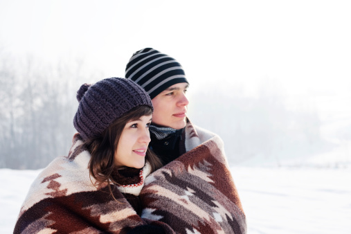 Young couple in winter looking away, under blanket
