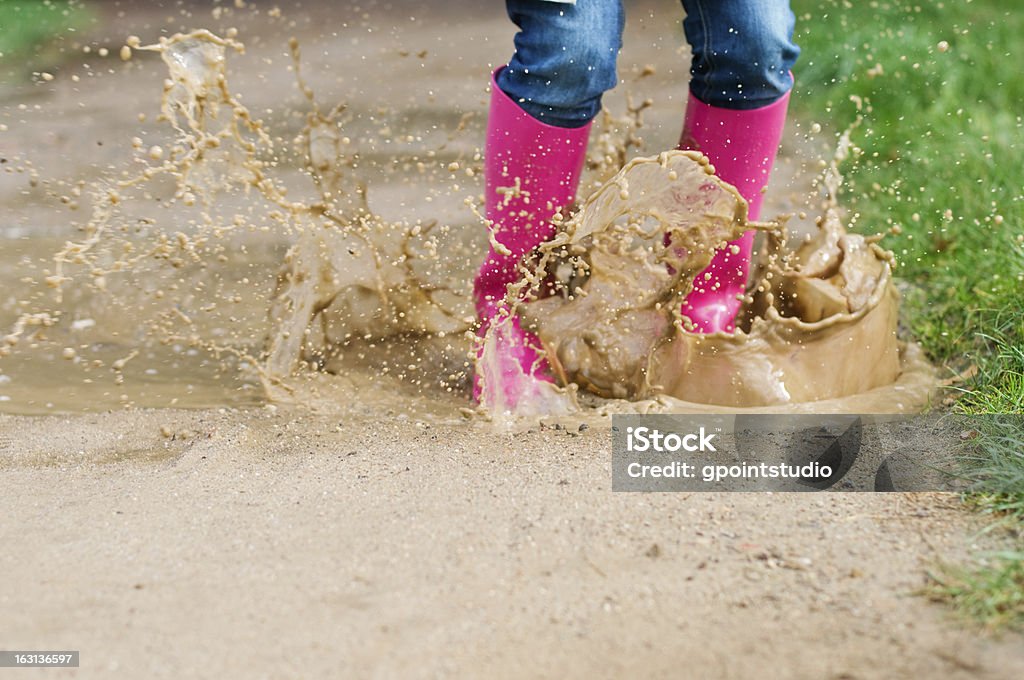 Young woman with rubber boots jumping in puddle Jeans Stock Photo