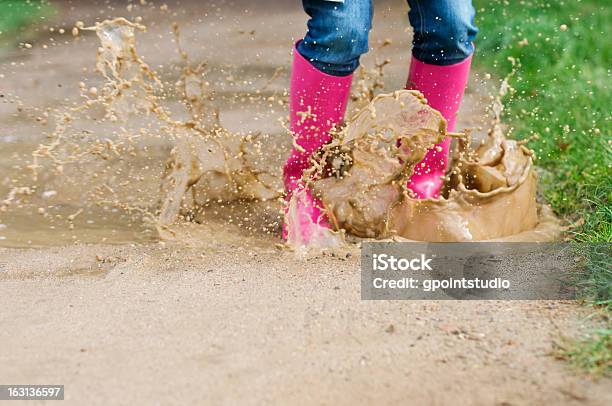Young Woman With Rubber Boots Jumping In Puddle Stock Photo - Download Image Now - Jeans, Jumping, Mud