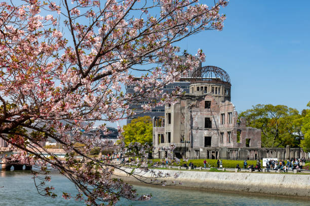 Hiroshima, Japan-April 9, 2023; View of the Atomic Bomb or Genbaku Dome along the river with Cherry Blossom tree in front Peace Memorial Park; iconic remains of the Industrial promotion hall