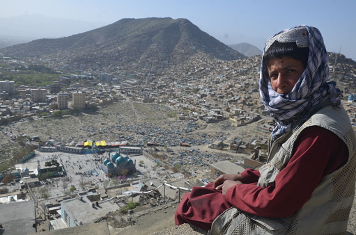 Salam hill is located in Kabul province of Afghanistan. A little kid sitting at the edge of a rock and looking downside to the city.
