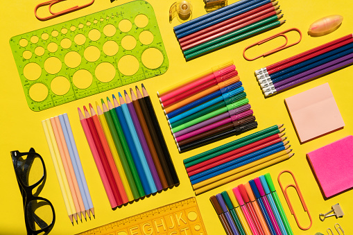 Top view of a large group of multi colored school or office supplies shot on rustic dark wooden table. A blank note pad is at the center of the composition with useful copy space ready for text and/or logo. DSRL studio photo taken with Canon EOS 5D Mk II and Canon EF 100mm f/2.8L Macro IS USM