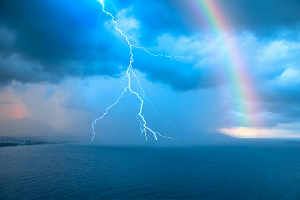 Stormy and rainy weather thunder and lightning strikes between clouds, rainbow in the background