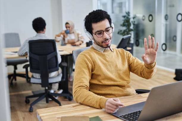 istock Young Middle Eastern man waving at camera during online meeting in office 1631428132