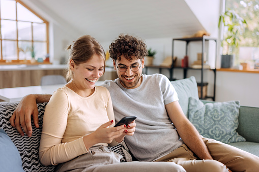 Young couple using phone together while sitting on a sofa at home