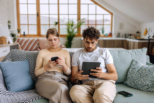 istock Couple using their own digital devices while sitting on a sofa at home 1631439184