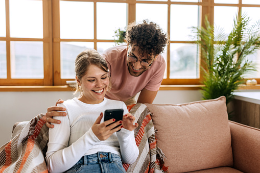 Young cheerful couple using smart phone at home