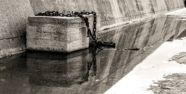 istock Concrete block with rusty chain on a puddle of stagnant water 1631444672