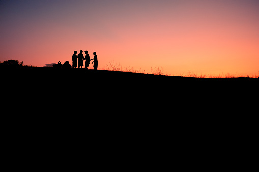 sunset silhouette of a group of 4 children friends playing together. concept of childhood friendship.