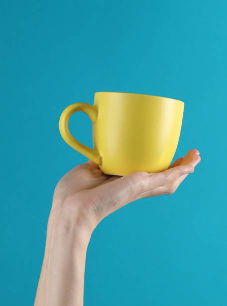 istock Woman's hand holds a yellow ceramic cup on a blue background 1631482030
