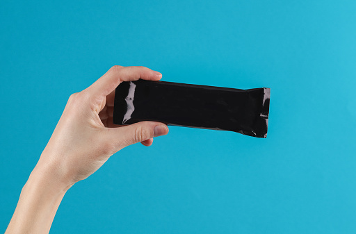 Hand holds a black pack of a bar or protein on blue background