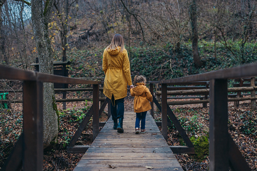 A woman and a little girl walking down the old bridge, discovering the forest, surrounded by beautiful nature.