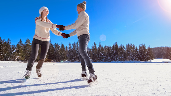 Smiling couple holding hands while ice skating on frozen lake.