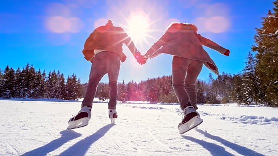 Rear view of couple holding hands while ice skating on frozen lake in winter.