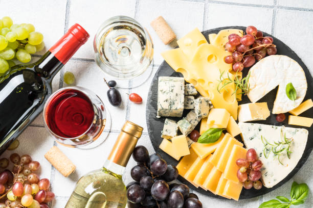 Cheese platter with craft cheese assortment and wine glasses at white tile background. Cheese platter with craft cheese assortment and wine glasses at white tile background. Top view. cheese wine food appetizer stock pictures, royalty-free photos & images