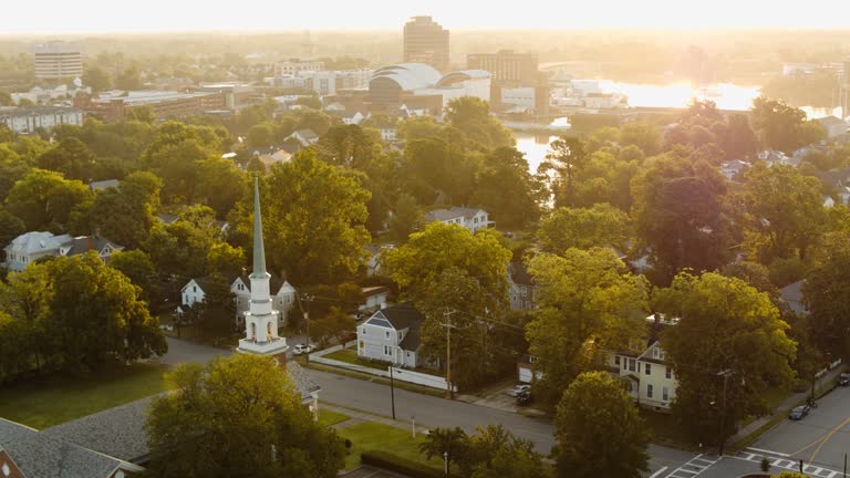 Sunny coastal townscape in early morning. Virginia Air & Space Science Center and NASA Langley visitor center in dawn horizon on Hampton River, VA. Aerial footage with orbiting-panning-tilt up from church and Residential Area camera motion