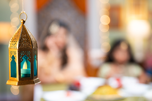 Close up shot of indain Muslim family to hanging lantern while eating during Ramadan iftar dinner at home - concept of holy month, Ramzan Kareem and festive celebration.
