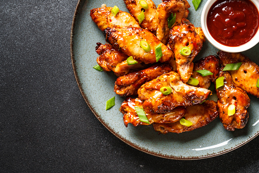 Chicken wings in bbq sauce on craft plate. Top view, close up on black stone table.