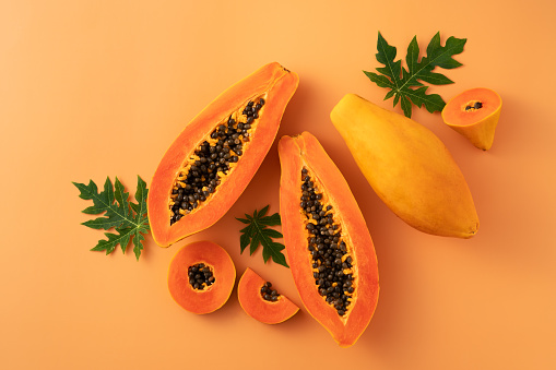 Cut Papaya over orange table background for tropical fruit design concept, top view copy space.