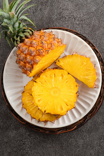 Top view of fresh cut pineapple with tropical leaves on gray table background.