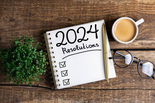 New year resolutions 2024 on desk. 2024 resolutions list with notebook, coffee cup on table. Goals, resolutions, plan, action, checklist concept. New Year 2024 template