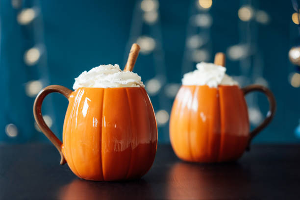暗い背景に黒いテーブルにホイップクリームと温かい飲み物のカボチャの形をしたカップ、シナモンスティック。スパイスとパンプキンラテ。感謝祭のための居心地の良い秋の飲み物、自宅� - latté pumpkin spice coffee ストックフォトと画像