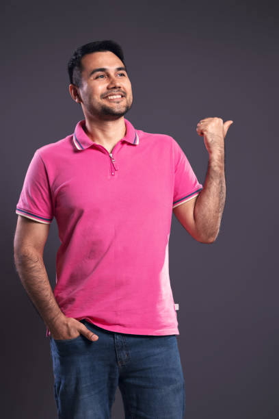 ritratto di un brasiliano che indossa una polo rosa, dal davanti, che indica di lato con il pollice della mano sinistra, e con la mano destra infilata nella tasca dei jeans, sorridente e guardando di lato - belém - pará - brasile - polo shirt flash foto e immagini stock