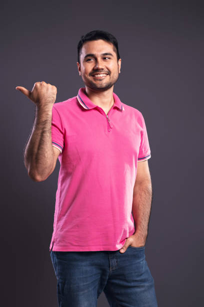 ritratto di un brasiliano che indossa una polo rosa, in posizione 3/4, indicando di lato con il pollice della mano destra e con la mano sinistra nella tasca dei jeans, sorridente e guardando di lato - belém - al brasile - polo shirt flash foto e immagini stock