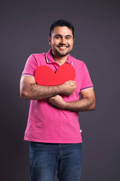 ritratto di un brasiliano che indossa una polo rosa, dal davanti, abbracciando un cuore di carta rossa, guardando la macchina fotografica e sorridendo - belém - pará - brasile - human heart flash foto e immagini stock