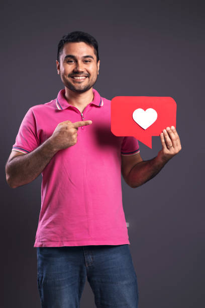 ritratto di un brasiliano che indossa una polo rosa, tenendo con la mano sinistra un fumetto con un cuore bianco all'interno, con la mano destra che lo indica, felice, guardando la macchina fotografica e sorridendo - belém - pará - brasile - polo shirt flash foto e immagini stock