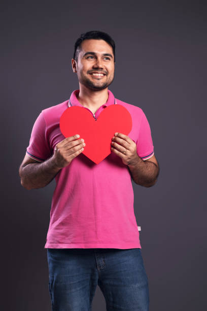 portrait of a brazilian wearing a pink polo shirt, from the front, holding a red paper heart with both hands, looking to the side and smiling - belém - pará - brazil - human heart flash imagens e fotografias de stock
