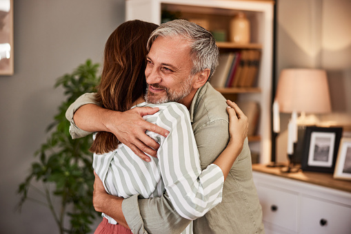 A cheerful caring man enjoying a hug with his loving adult daughter at his cozy home.