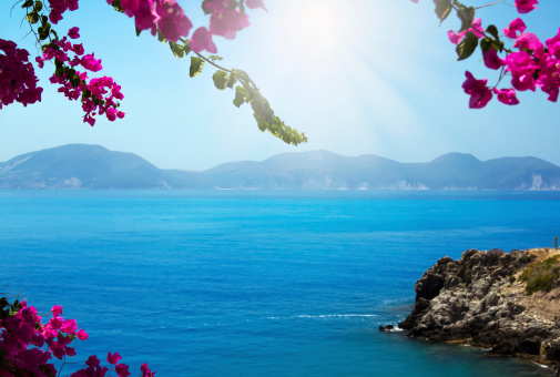 Pink flowers (bougainvillea) blooming at Kefalonia island, Greece, framing the blue Mediterranean Sea. Focus is on the flowers, The sea is slightly out of focuse and it may be used as copy space.